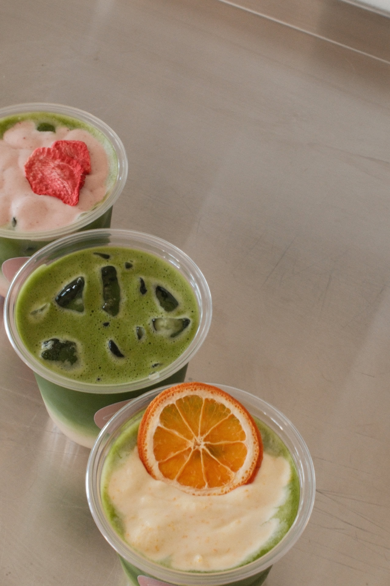 Three iced matcha drinks with strawberry and orange toppings